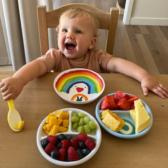 Niño pequeño jugando con platos de colores llenos de frutas y verduras